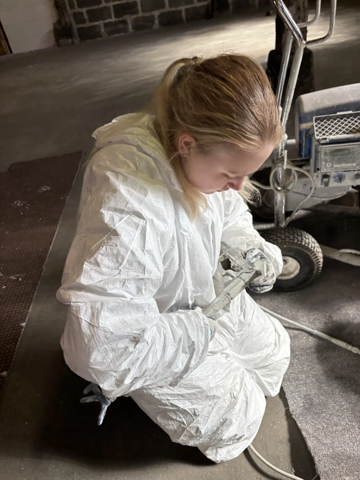 Marie kniet an der Airless-Anlage und bereitet das Gerät vor