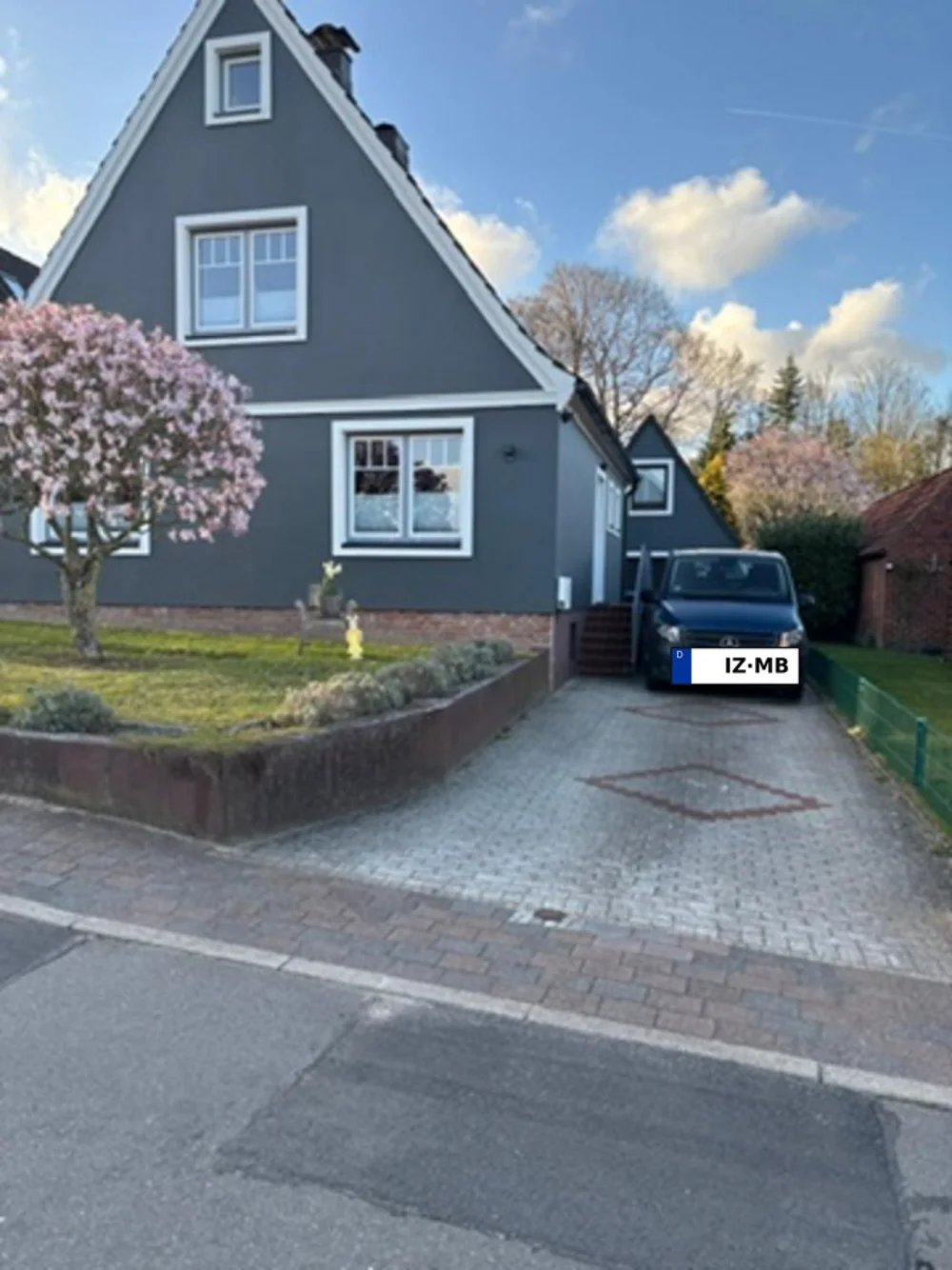 Die fertig gestaltete Fassade in Anthrazit mit weißen Zierelementen, davor eine blühende Magnolie